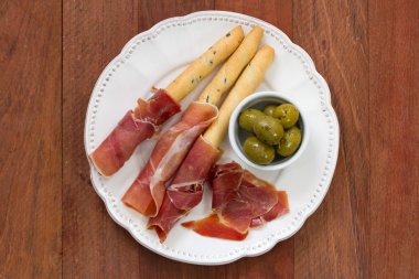 Prosciutto kahverengi zemin üzerine beyaz tabakta zeytinli