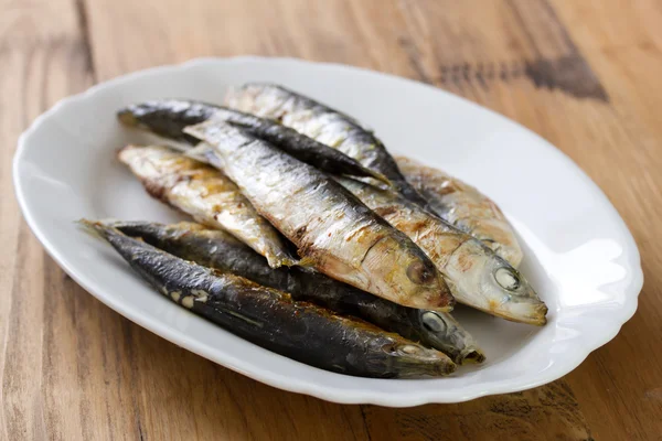 Sardine fritte su piatto bianco su fondo di legno marrone — Foto Stock