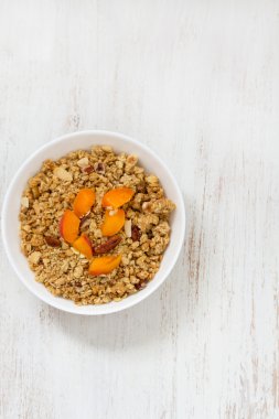 Granola with fruits and nuts in white bowl on wooden background