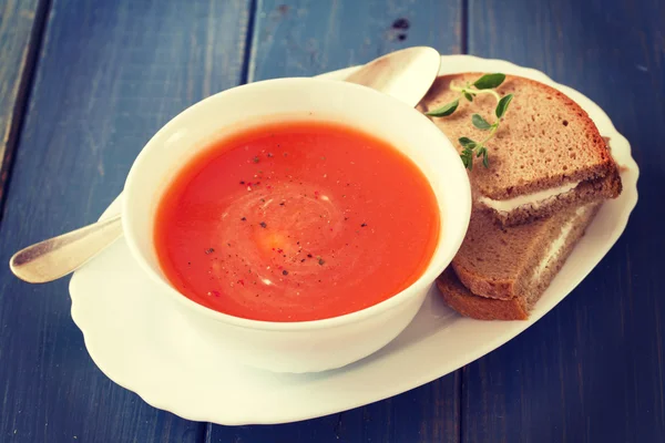 Tomatensuppe in weißer Schüssel mit Sandwich auf blauem Holzhintergrund — Stockfoto