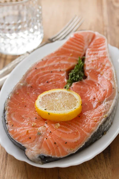 Fresh salmon with lemon on white dish on brown wooden background — Stock Photo, Image