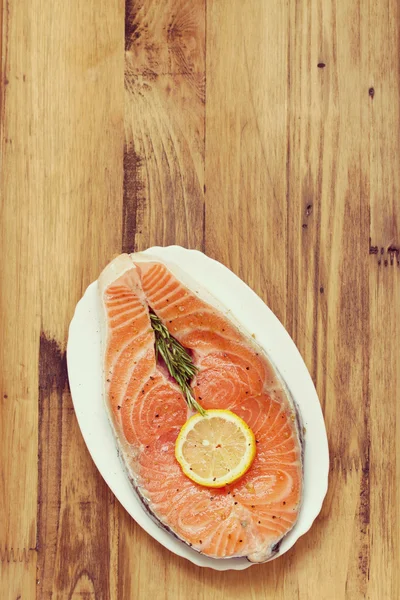 Свежий лосось с лимоном на белом блюде на коричневом деревянном фоне — стоковое фото