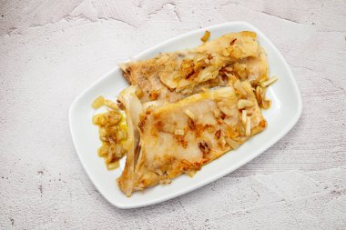 Beyaz tabakta soğan ve biberli kızarmış morina balığı.