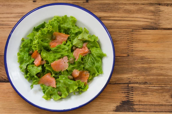 Salad with smoked salmon on plate on brown background — Stock Photo, Image