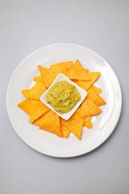 Meksika cipsi ve kâse ev yapımı avokado sosu ve beyaz tabakta limon.