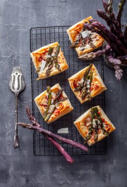 Kapalı fotoğraf setinde mor kuşkonmaz taze sebzeler ve koyu arkaplanda lezzetli poğaça turtaları var. Resimler, yemek tarifleri ile ilgili temalar için uygun gurme malzemelerini, rustik dokuları ve yaratıcı yiyecek sunumunu gösteriyor.
