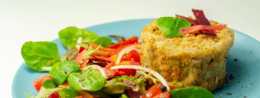 Eriyen çedar soslu füme mezgit balığı keki ve mavi tabakta karışık salata, deniz ürünleri.