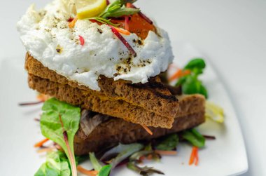 Izgara sandviçlerin üstünde yumurta, sosis, domates ve mayonez, hepsi taze salata ve lezzetli bir kahvaltıyla servis ediliyor.