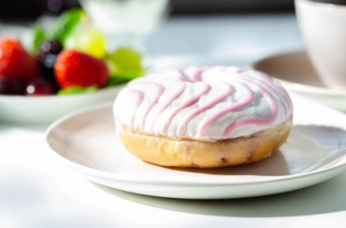 Kahve ve taze meyvelerle servis edilen beyaz ve pembe kremalı lezzetli donut, tatlı bir sabah.