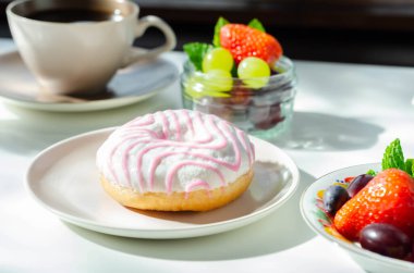Kahve ve taze meyvelerle servis edilen beyaz ve pembe kremalı lezzetli donut, tatlı bir sabah.