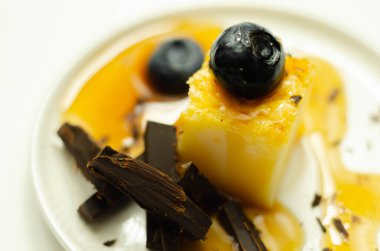 Bir porsiyon vanilyalı cheesecake yaban mersini ve sütlü çikolatayla süslenmiş, üzerine karamel sosu, tatlı bir mola.