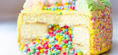 Sarı krema kaplı Madeira süngeri, erik ve ahududu reçeli katmanlı, çok renkli çikolata parçacıkları ile doldurulmuş ve üzeri çok renkli dondurmalar ve şeker süslemeleri ile süslenmiş, pinata keki.