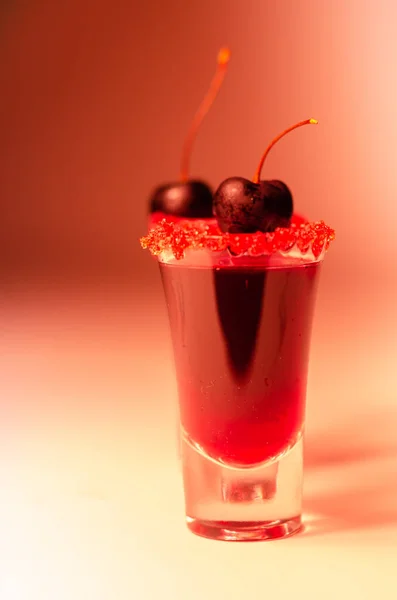 Ruby red cocktail based on vodka, cherry liqueur and syrup in drink shot glass, decorated with fresh cherry and red sugar, sweet drink