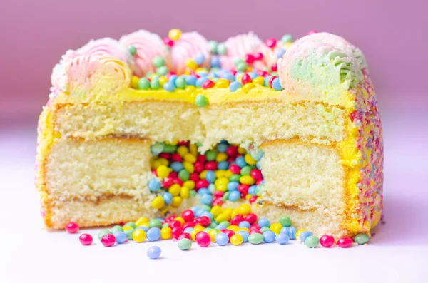 Madeira sponge coated with yellow colour frosting, layered with plum and raspberry jam, filled and topped with multicolour chocolate nibs and decorated with multicolour frostings and sugar decorations, pinata cake