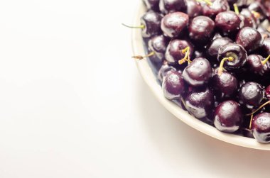 Beyaz seramik bir tabakta taze ve olgun kirazlar, sulu meyveler