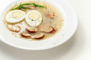 Geleneksel Polonya ekşi çorbası sosis ve yumurta ile birlikte beyaz bir tabakta, Doğu Avrupa yemeği.