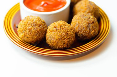 Yanında kırmızı sos olan bir tabak kızarmış yemek. Yemek küçük ve yuvarlak, sos da beyaz bir kasenin içinde.