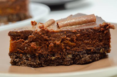 Üstünde altın dekoru olan bir dilim çikolatalı pasta. Pasta kesilip beyaz bir tabağa konur.