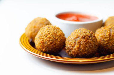 Yanında kırmızı sos olan bir tabak kızarmış yemek. Yemek küçük ve yuvarlak, sos da beyaz bir kasenin içinde.