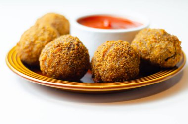 Yanında kırmızı sos olan bir tabak kızarmış yemek. Yemek küçük ve yuvarlak, sos da beyaz bir kasenin içinde.