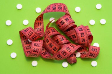 Ölçüm bandı beyaz yuvarlak tabletlerle çevrili yeşil arkaplanda. Foto farmakolojik kilo kaybı ve sibutramin, orlistat, metformin gibi ilaçların kullanımı