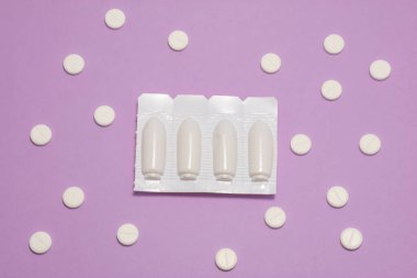 Vajinal ya da rektal fitilli plastik ambalaj mor arka planda polka noktalarıyla süslenmiş yuvarlak tabletlerle çevrilidir. Proktolojik ya da jinekolojik fotoğraf tedavisi kavramı