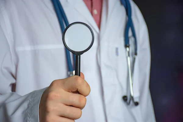白衣を背景に手に虫眼鏡をかけた医師 病気の診断と検索のための概念写真 — ストック写真