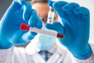 Doktor ya da bilim adamı bir elinde laboratuvar tüpünde kan, metin ya da patojen yazıtları için temiz bir yer ve aşı ya da ilaç içeren şeffaf bir şişe tutuyor.