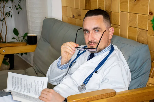 Doctor caucasian with book in his hands and phonendoscope around his neck is resting,  studying new disease or method of medical diagnostics in hospital break room