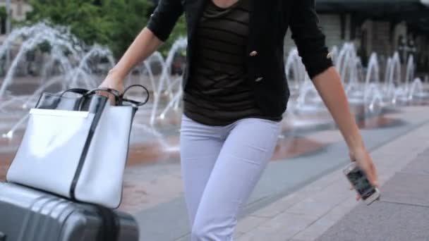 Kvinna med resväska på plaza med jet fontäner — Stockvideo