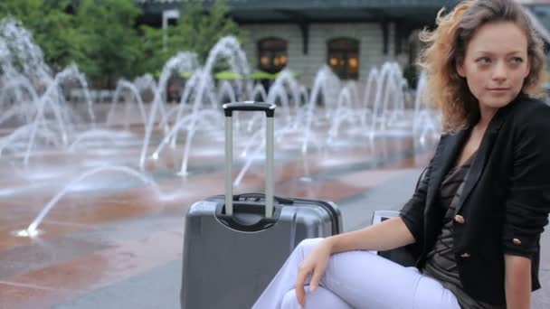 Kvinna med resväska på plaza med jet fontäner — Stockvideo