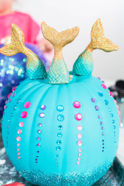 Little girl decorating her Halloween pumpkin with glitter.