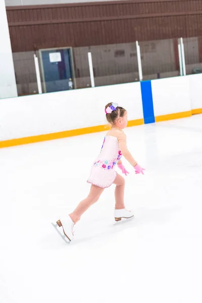 穿着漂亮粉红裙子的小女孩在室内溜冰场上练习花样滑冰 — 图库照片