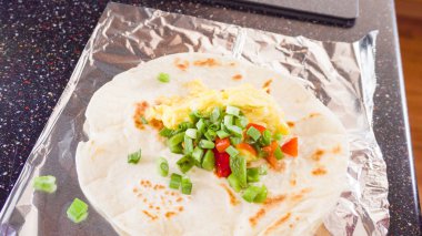 Un tortilla içinde taze sebze, yumurta ve pastırma ile kahvaltıda burrito pişirmek..