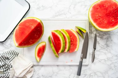 Beyaz bir kesme tahtasının üzerinde çekirdeksiz kırmızı karpuz dilimliyorum..
