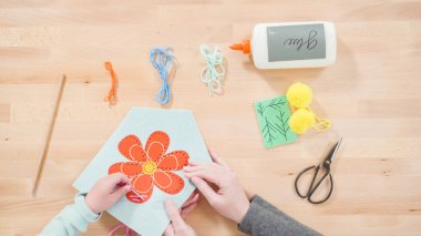 Küçük kız annesiyle el sanatları masasında dikiş dikmeyi öğreniyor..