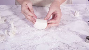 Adım adım. Mermer tezgahın üzerindeki beyaz fondanla kar tanelerini keserek..