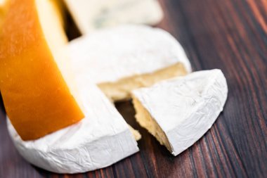 Koyu ahşap arka planda büyük gurme peynir dilimleri var..