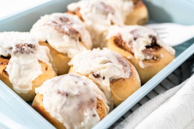 Taze pişmiş tarçınlı rulo, beyaz kremalı, mavi bir tavada..