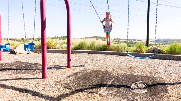 郊外の子供の遊び場でスイングで遊んでいる女の子 — ストック写真