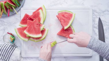 Düz yatıyordu. Kırmızı karpuzu beyaz bir kesme tahtasının üzerinde küçük parçalara ayırmak.