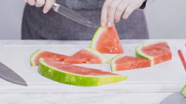 Kırmızı karpuzu beyaz bir kesme tahtasının üzerinde küçük parçalara ayırmak.