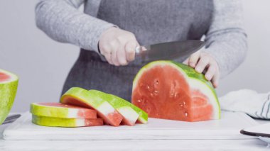 Kırmızı karpuzu beyaz bir kesme tahtasının üzerinde küçük parçalara ayırmak.