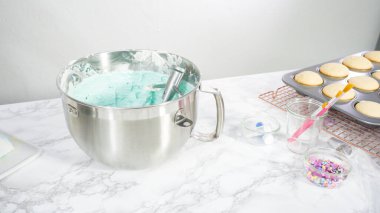 Adım adım. Denizkızı temalı vanilyalı kekler için tereyağlı krema yapmak için mutfak mikserinde malzemeler karıştırılıyor..