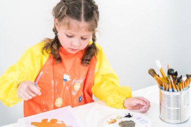 Evde akrilik boyalı bir sanat projesi üzerinde çalışan küçük bir kız..