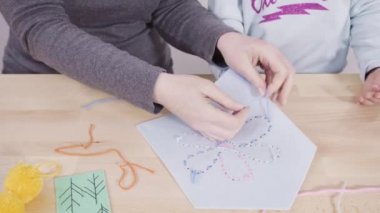 Küçük kız annesiyle el sanatları masasında dikiş dikmeyi öğreniyor..