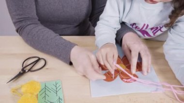 Küçük kız annesiyle el sanatları masasında dikiş dikmeyi öğreniyor..