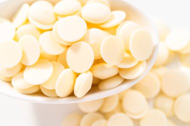 Beyaz arka planda çikolata şekillerini eritmek için beyaz yuvarlak çikolata parçaları..