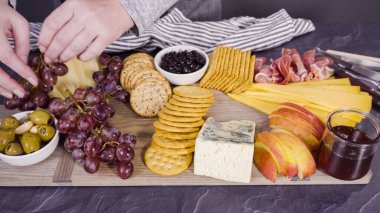 Arranging gourmet cheese, crakers, and fruits on a board for a large cheese board. clipart