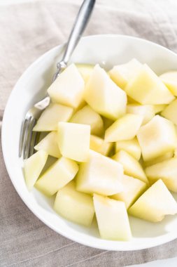 Beyaz bir kasede dilimlenmiş altın çiğ taneli kavun..